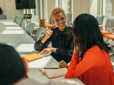 Image of two women in a board room. One woman is signing to the other woman.