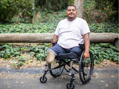 Stock photo of a man who is a a person with amputations using a wheelchair in an outdoor setting, smiling.